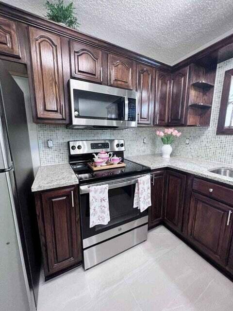 kitchen featuring decorative backsplash, light stone countertops, stainless steel appliances, dark brown cabinets, and open shelves