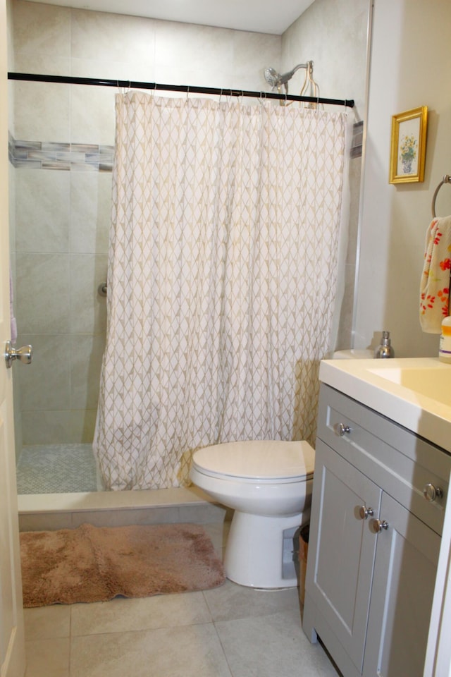 bathroom featuring toilet, vanity, a tile shower, and tile patterned floors