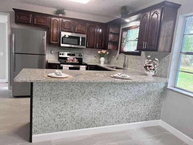 kitchen with appliances with stainless steel finishes, a sink, a peninsula, and dark brown cabinetry