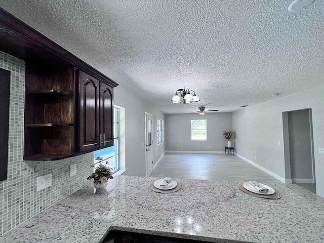 kitchen with baseboards, open floor plan, dark brown cabinets, light stone countertops, and tasteful backsplash