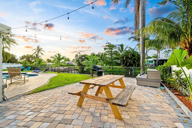 patio terrace at dusk with outdoor dining area, grilling area, a fenced backyard, and a fenced in pool