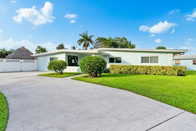 ranch-style home featuring fence, concrete driveway, a gate, stucco siding, and a front lawn