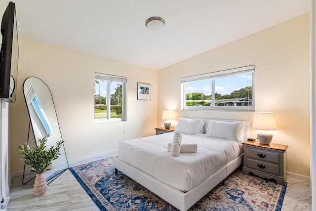 bedroom featuring lofted ceiling, marble finish floor, and baseboards