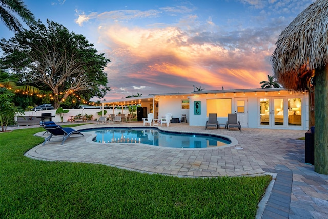 pool at dusk featuring a fenced in pool, a lawn, a patio, fence, and french doors