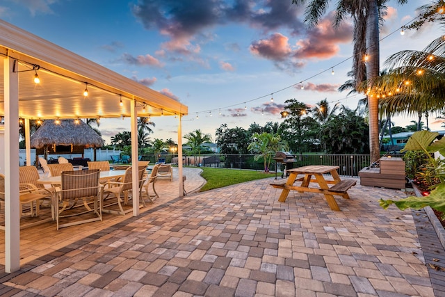 patio terrace at dusk with fence, outdoor dining area, and a gazebo