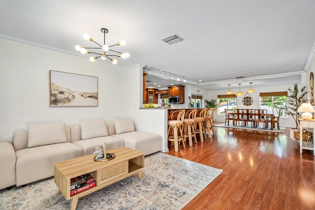 living room with crown molding, a notable chandelier, visible vents, a textured ceiling, and wood finished floors