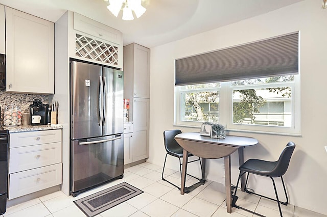 kitchen featuring light tile patterned floors, light stone counters, backsplash, and freestanding refrigerator