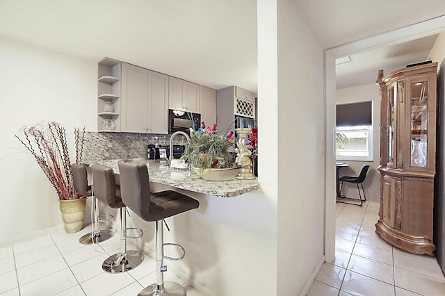 kitchen with black microwave, a breakfast bar area, decorative backsplash, light tile patterned flooring, and open shelves