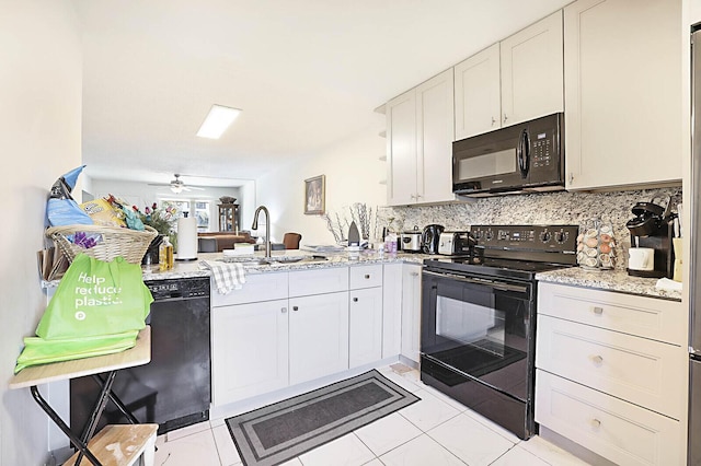 kitchen with light stone counters, a peninsula, a sink, decorative backsplash, and black appliances