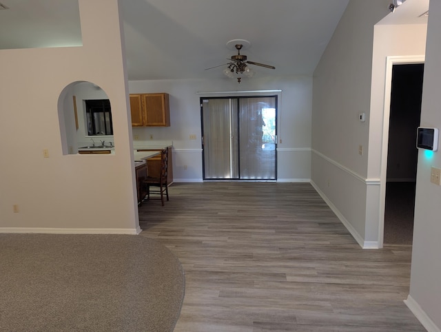 interior space featuring ceiling fan, a sink, light wood finished floors, arched walkways, and baseboards