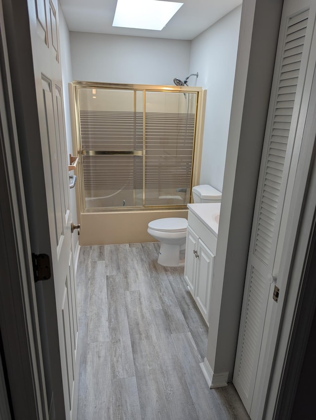 bathroom with a skylight, wood finished floors, vanity, toilet, and enclosed tub / shower combo