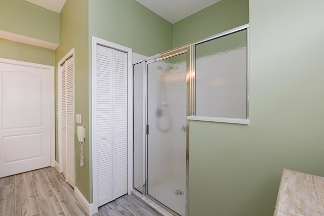 full bathroom featuring a closet, baseboards, wood finished floors, and a shower stall