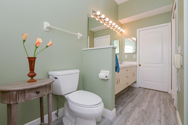 bathroom featuring baseboards, toilet, wood finished floors, and vanity