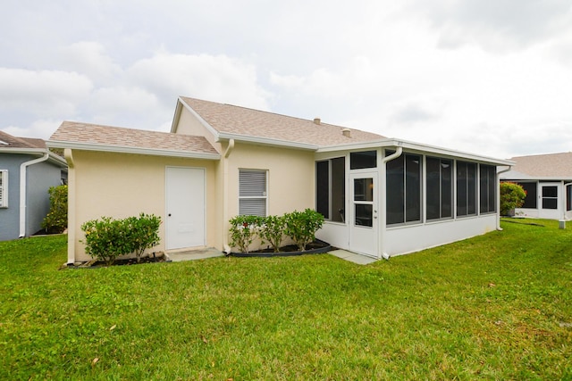 back of house with a yard, roof with shingles, stucco siding, and a sunroom