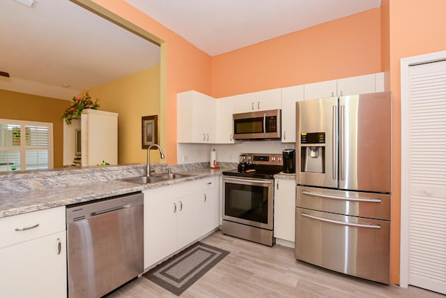 kitchen with light stone countertops, light wood finished floors, a sink, stainless steel appliances, and white cabinets