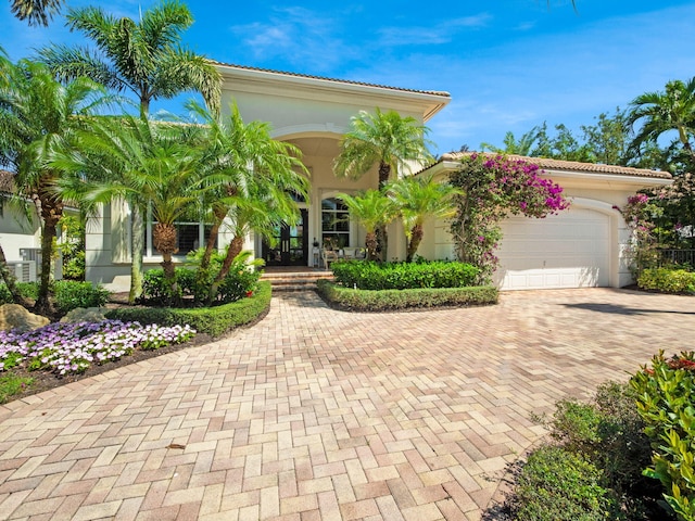 mediterranean / spanish home featuring stucco siding, decorative driveway, a porch, a garage, and a tiled roof