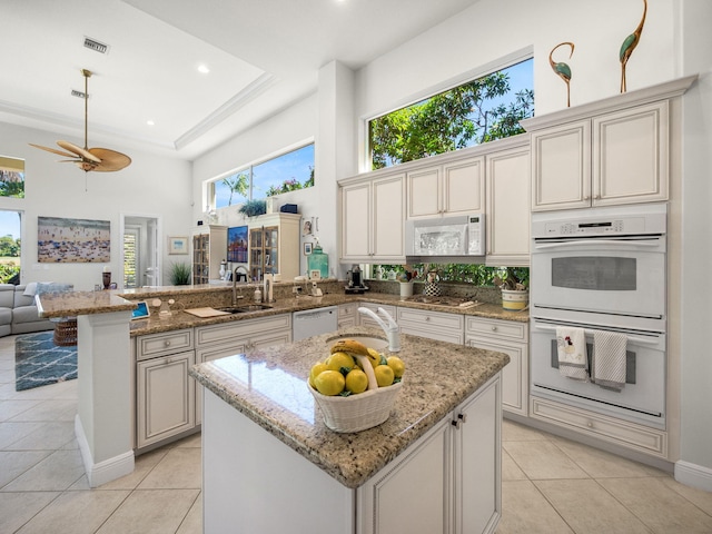 kitchen with a sink, open floor plan, white appliances, a peninsula, and light tile patterned floors