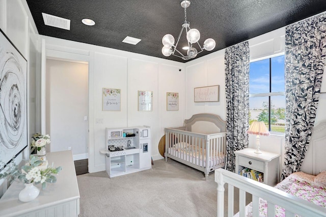 carpeted bedroom with a notable chandelier, visible vents, a textured ceiling, and a nursery area