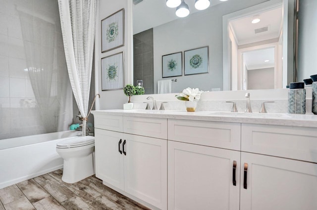 bathroom featuring visible vents, toilet, double vanity, wood finished floors, and a sink