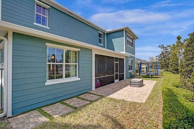 back of house featuring a patio, a trampoline, a lawn, and a sunroom