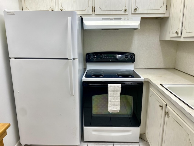 kitchen with under cabinet range hood, light countertops, range with electric stovetop, freestanding refrigerator, and a sink