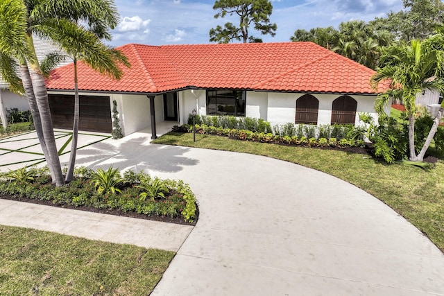 mediterranean / spanish-style house with a tiled roof, concrete driveway, a front yard, stucco siding, and a garage