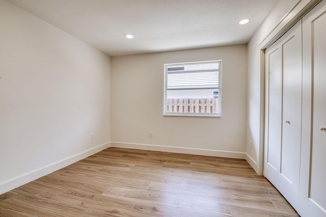 unfurnished bedroom featuring light wood-style flooring, baseboards, and a closet