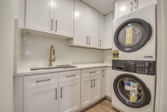 laundry area featuring light wood-style floors, a sink, cabinet space, and stacked washer / drying machine