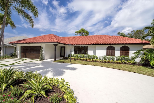 mediterranean / spanish house featuring driveway, a tiled roof, an attached garage, and stucco siding