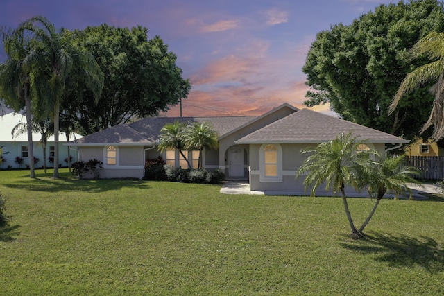 ranch-style home featuring a yard, a shingled roof, and stucco siding