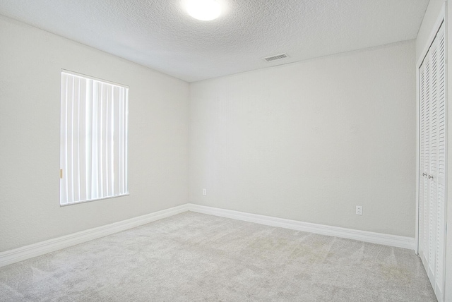 empty room featuring a textured ceiling, carpet flooring, visible vents, and baseboards