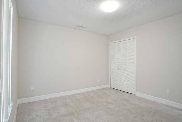 unfurnished bedroom featuring a closet, visible vents, light carpet, a textured ceiling, and baseboards