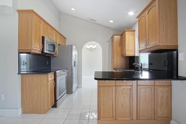 kitchen with arched walkways, a peninsula, a sink, vaulted ceiling, and appliances with stainless steel finishes