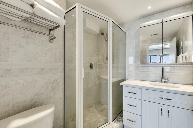 bathroom featuring toilet, visible vents, vanity, tile walls, and a stall shower