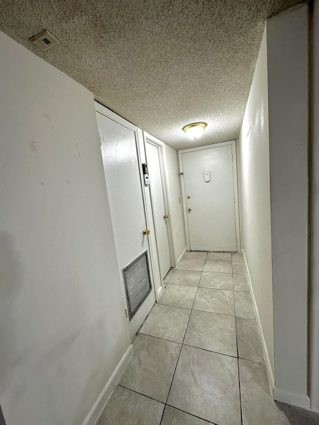 corridor featuring light tile patterned floors, visible vents, baseboards, and a textured ceiling