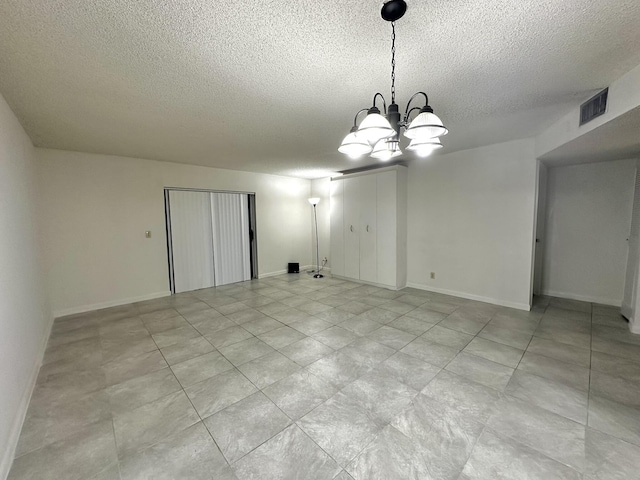 unfurnished room featuring a textured ceiling, a notable chandelier, visible vents, and baseboards