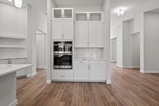 kitchen with light countertops, stainless steel double oven, wood finished floors, and white cabinets