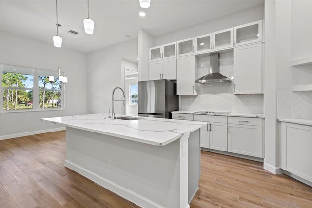 kitchen featuring black electric stovetop, a sink, freestanding refrigerator, decorative backsplash, and wall chimney exhaust hood