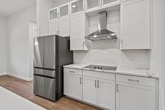 kitchen with black electric stovetop, freestanding refrigerator, white cabinets, wall chimney range hood, and wood finished floors