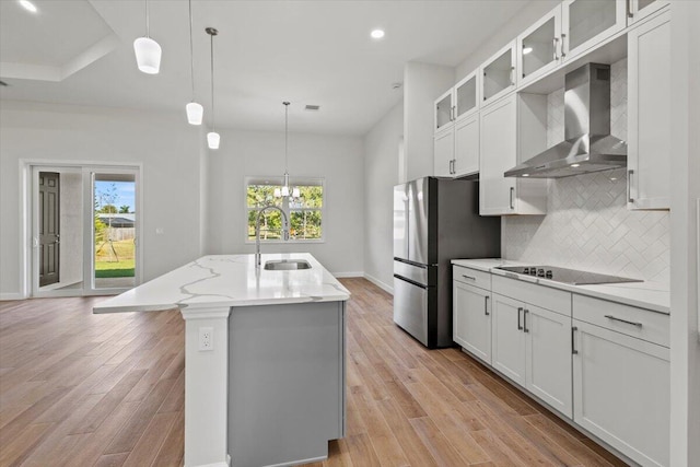 kitchen featuring decorative backsplash, freestanding refrigerator, a sink, wall chimney exhaust hood, and black electric cooktop