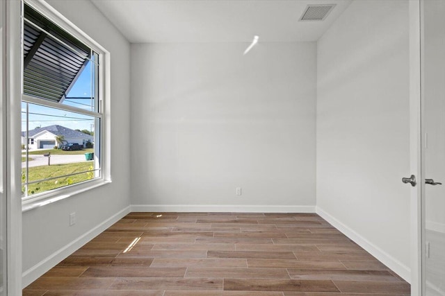 empty room with wood finished floors, visible vents, and baseboards