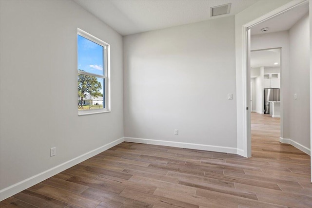 unfurnished room with wood finished floors, visible vents, and baseboards