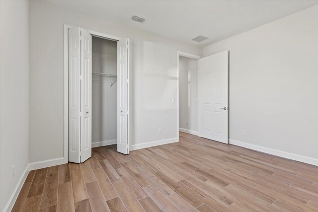 unfurnished bedroom featuring light wood-type flooring, baseboards, visible vents, and a closet