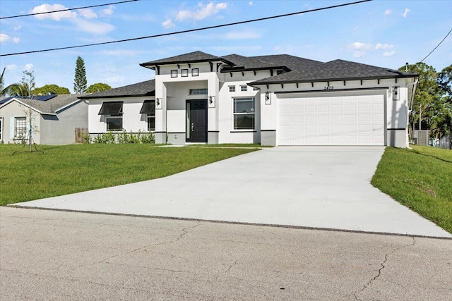 prairie-style house featuring a garage, a shingled roof, concrete driveway, a front yard, and stucco siding