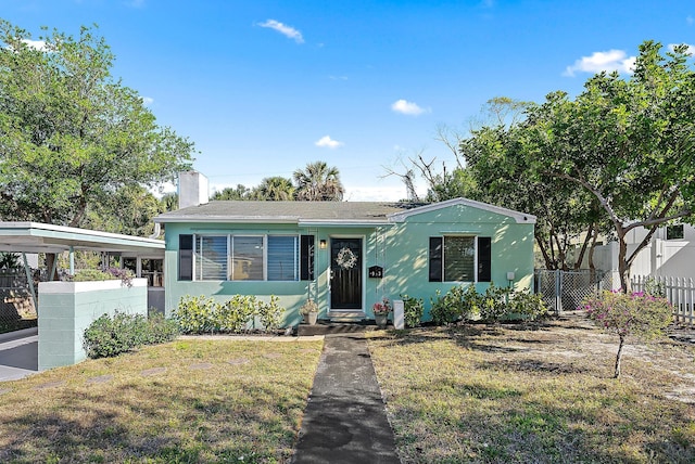 view of front of property featuring a front yard, fence, a chimney, stucco siding, and a carport