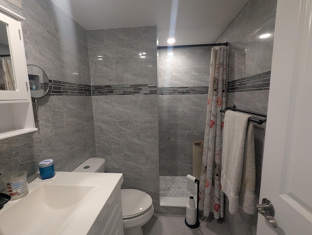 bathroom with a tile shower, vanity, toilet, and tile walls