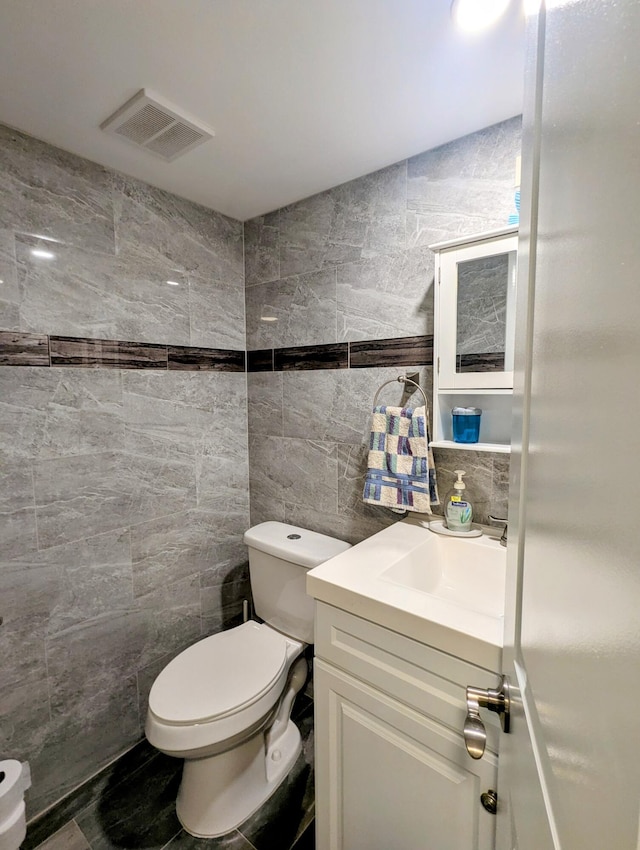 half bathroom with visible vents, toilet, tile walls, and vanity