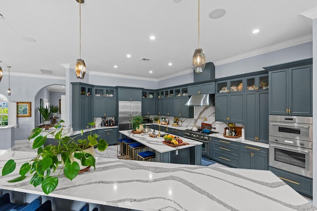 kitchen with visible vents, an island with sink, arched walkways, under cabinet range hood, and premium appliances