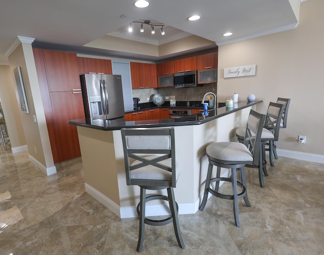 kitchen with crown molding, a tray ceiling, a kitchen breakfast bar, appliances with stainless steel finishes, and a peninsula