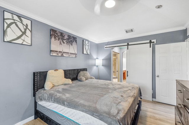 bedroom featuring visible vents, light wood-style flooring, a barn door, ornamental molding, and baseboards